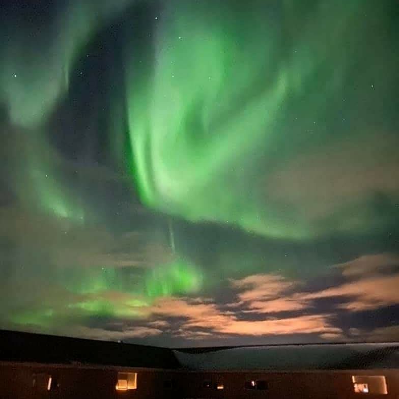 Aurora Borealis lights up the night sky with vibrant green swirls above silhouetted buildings.