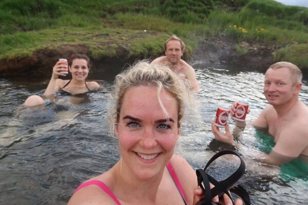 Group enjoying drinks in a scenic hot spring, surrounded by lush greenery and smiling at the camera.