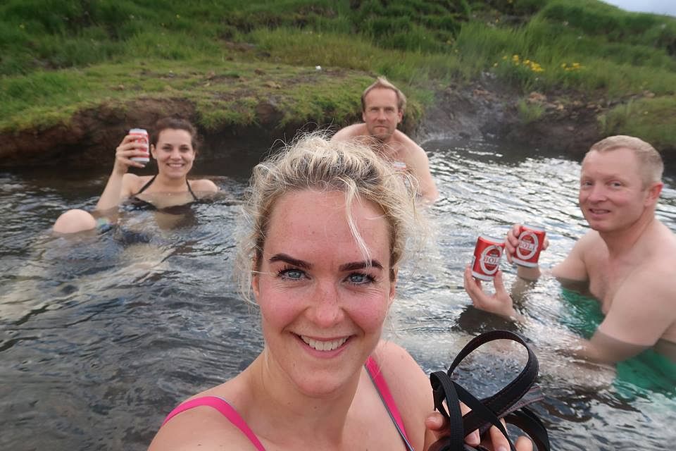 Group enjoying drinks in a scenic hot spring, surrounded by lush greenery and smiling at the camera.