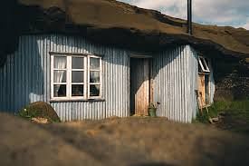 A rustic, corrugated metal house with a wooden door and multiple windows under a blue sky.