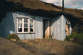 Rustic house with corrugated metal walls and turf roof on a sunny day.