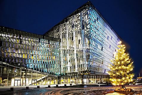 Modern glass building illuminated at night, with a festive Christmas tree in the foreground, under a dark blue sky.