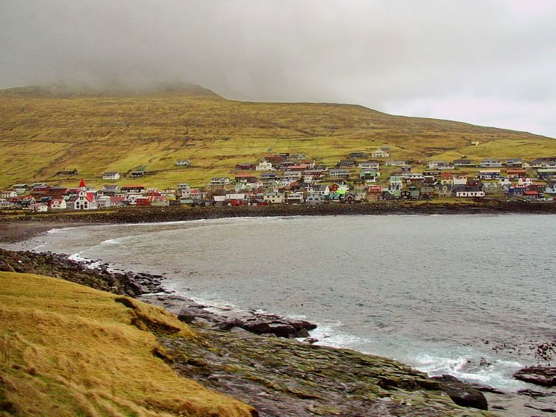 Scenic coastal village with colorful houses on a misty hillside by the sea, under a cloudy sky.