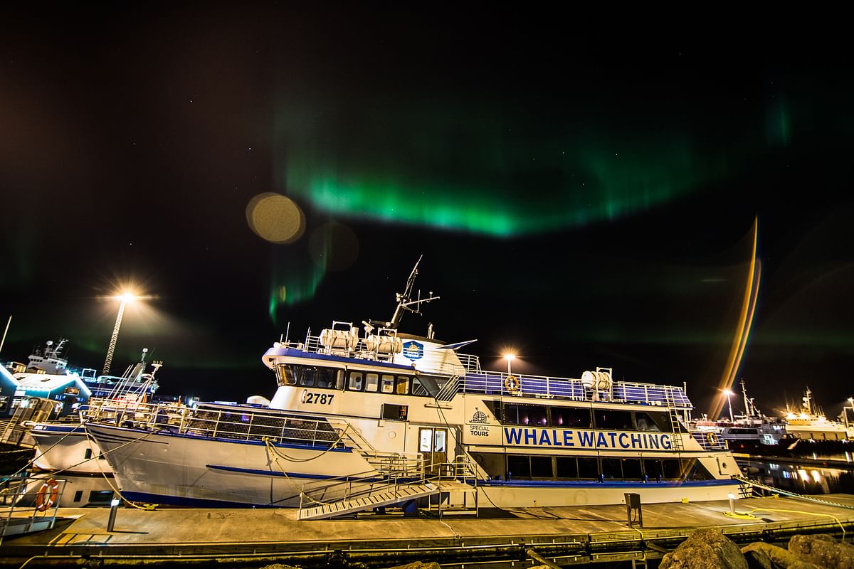 Whale watching boat docked under vibrant Northern Lights at night, perfect for an Arctic adventure.