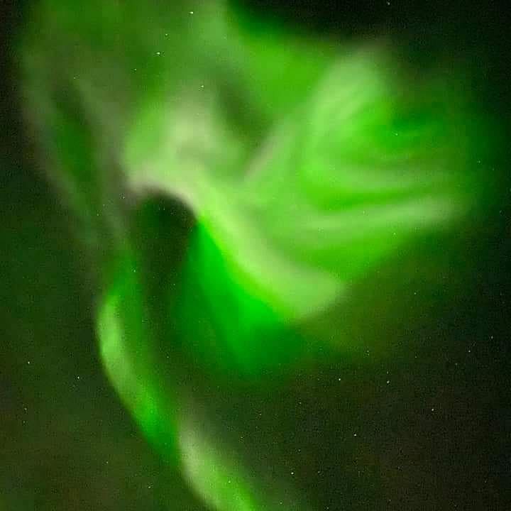 Green northern lights shimmering in the night sky, creating a mesmerizing aurora display with swirling patterns.