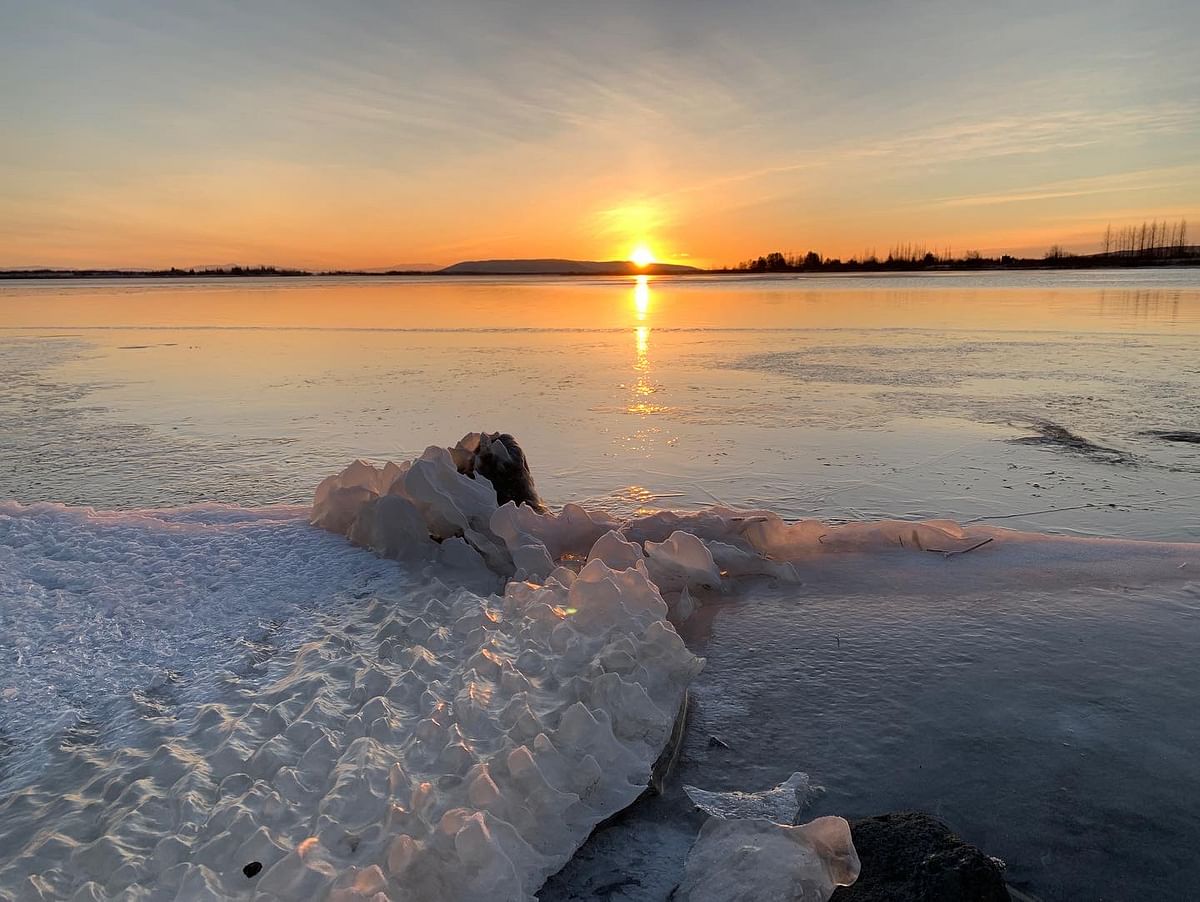 Frozen lake at sunset with icy shoreline and glowing horizon.