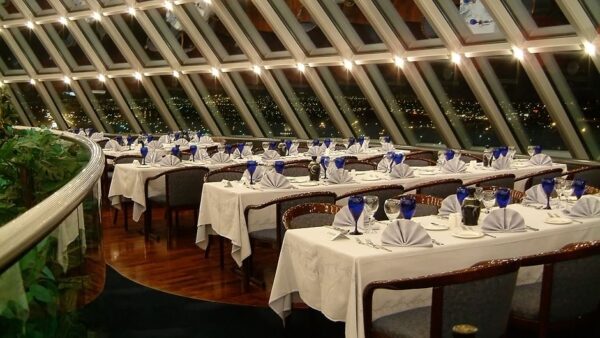 Elegant restaurant with panoramic window view, set tables, and ambient lighting at night.