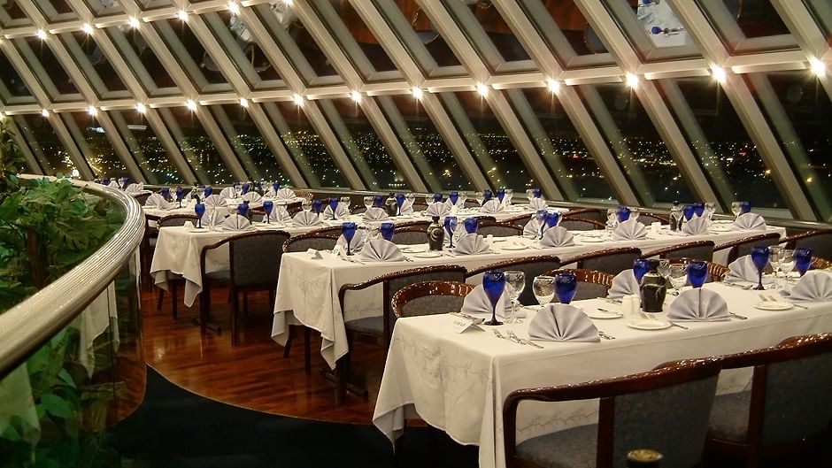 Elegant restaurant with panoramic window view, set tables, and ambient lighting at night.