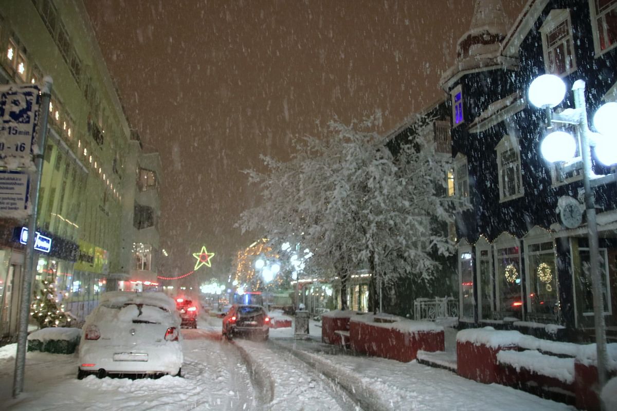 Snowy night street scene with decorated buildings, cars, and a lit star, capturing a festive, winter atmosphere.