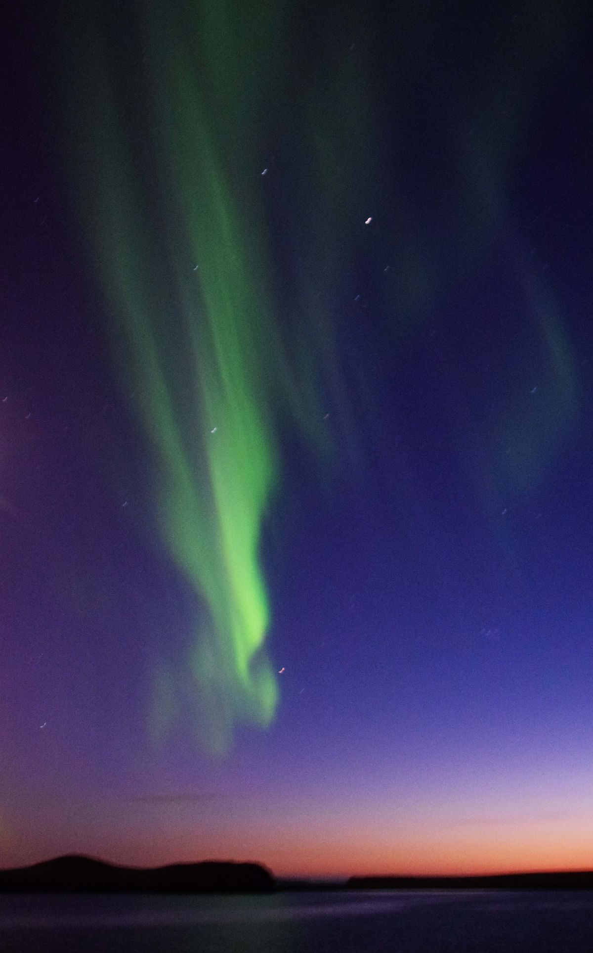 Aurora borealis lights dancing across a twilight sky over a serene lake and silhouetted mountains.
