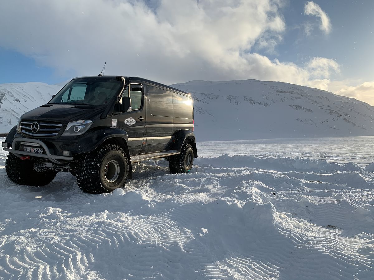 Black off-road van on a snowy landscape with mountain backdrop, highlighting winter adventure and rugged terrain capability.