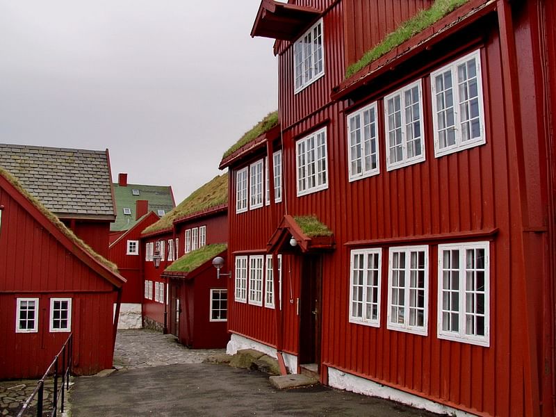 Red wooden houses with grass rooftops in the Faroe Islands, lined along a stone path under a cloudy sky.