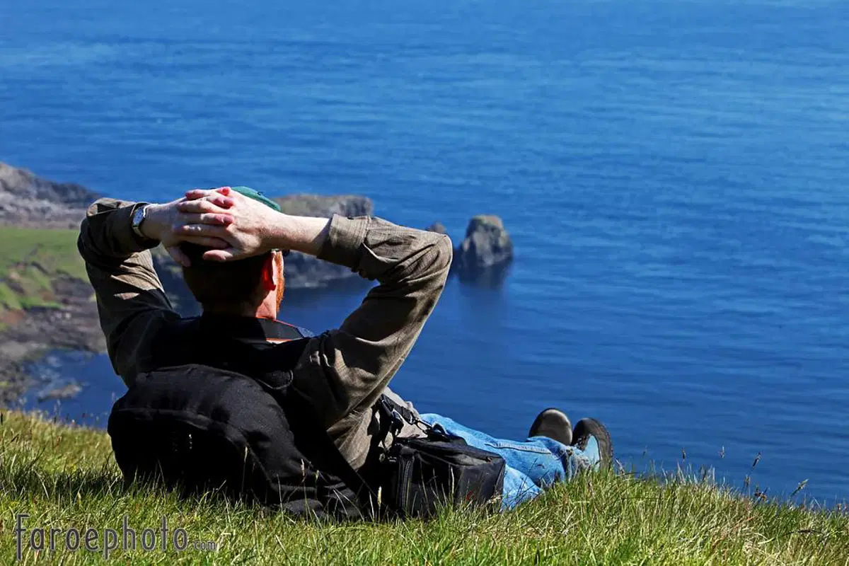 Man relaxing on grassy hill overlooking ocean, enjoying scenic coastline view.