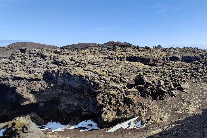 Rocky volcanic landscape under a clear blue sky, showcasing rugged terrain and sparse vegetation.
