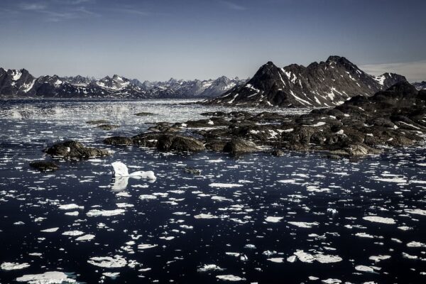 Mountainous Arctic landscape with icebergs floating in dark sea under a clear blue sky.