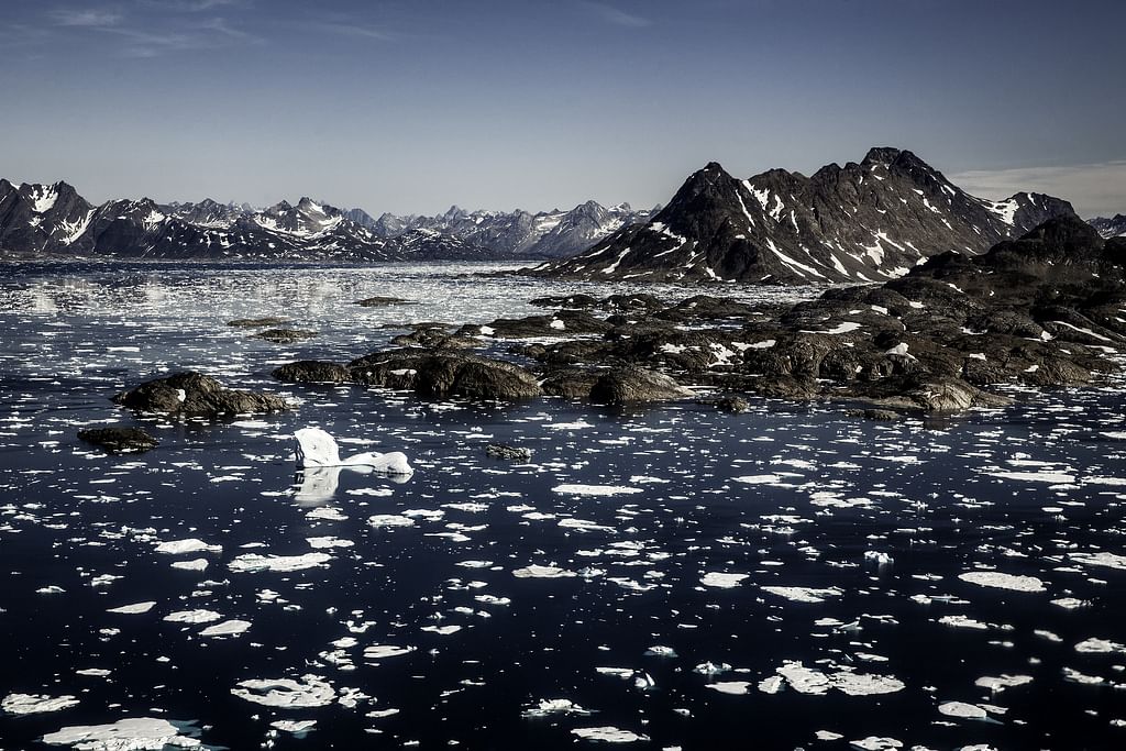 Mountainous Arctic landscape with icebergs floating in dark sea under a clear blue sky.