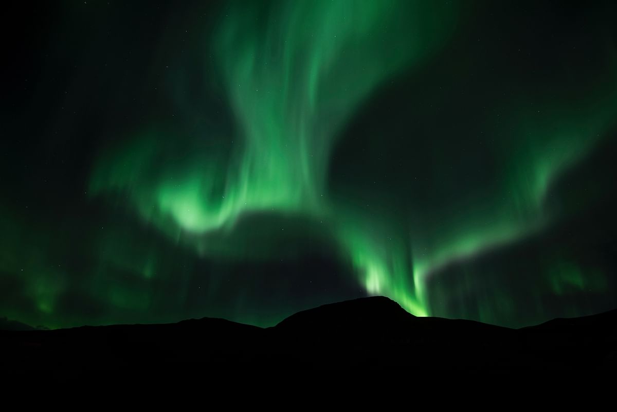 Aurora Borealis illuminating night sky over dark mountain silhouette.